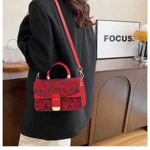 Détail du sac à main brodé rouge avec poignée tissée et fermoirs dorés porté par un mannequin