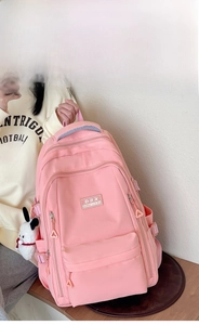 Side view of a light pink waterproof nylon backpack with multi-compartments and plush charm
