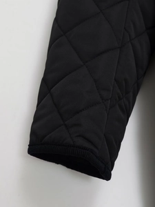 Nahaufnahme der schwarzen Steppjacke am Ärmel mit Rautenmuster und geripptem Saum