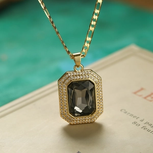 Macro shot of gold square pendant with dark grey gemstone on a vintage notebook