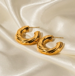 Polished 18K gold plated twisted C-shape hoop earrings on elegant silk fabric background