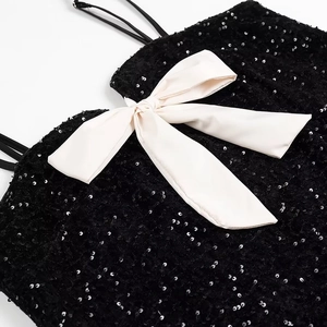 Detail of black sequined dress featuring a large white satin bow and delicate straps