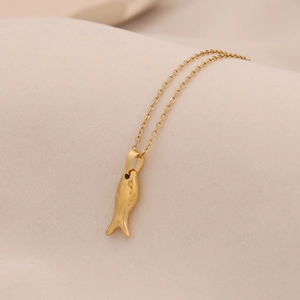 Close-up of a small golden fish pendant on a fine O-chain necklace over beige fabric
