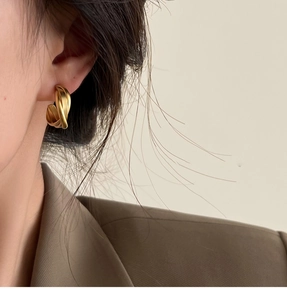Détail d'un clip d'oreille géométrique torsadé doré mat sur un mannequin en costume