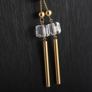 Macro shot of long gold sweater necklace featuring clear cube crystal and metal cylinder