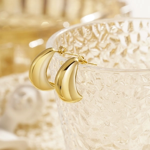 Polished gold horn C-shaped drop earrings hanging on a glass rim in warm light