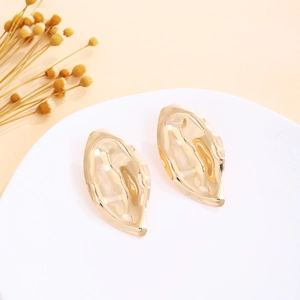 Close-up of golden irregular flame-shaped earrings with unique hammered texture on white tray