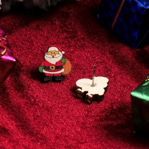 Close-up of Santa Claus wooden stud earrings on red velvet with festive gift boxes