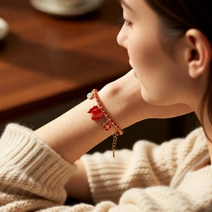 Detail of red beaded bracelet with 18k gold lucky bag pendant on female model wrist