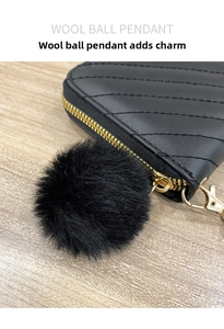 Detail of black quilted leather wallet with fluffy wool ball pendant and gold zipper