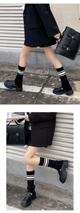 Close-up of black knitted leg warmers with white stripes paired with leather loafers