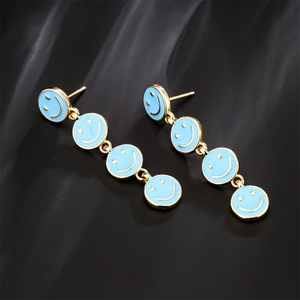 Long gold earrings with light blue enamel smiley face pendants on silk background