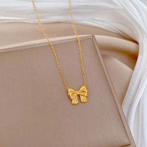 Detailed view of a gold bow pendant necklace resting on a beige jewelry box with silk