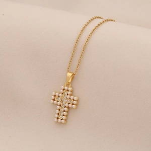 Detail of gold cross pendant with imitation pearls and rhinestones on beige fabric