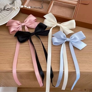 Set of four satin bow hair clips in pink, black, white, and light blue on a table