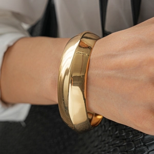 Close-up of a wide polished gold bangle with mirror finish on a model wearing white