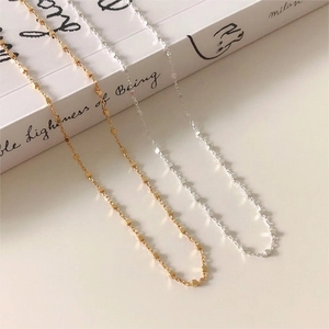 Close-up of minimalist gold and silver beaded cube necklaces on a book background