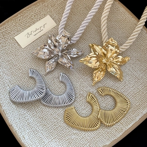 Flat lay of gold and silver flower necklaces with striped C-shape earrings on ceramic tray