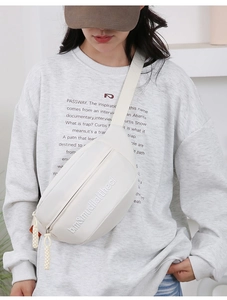 Detail of white canvas crossbody chest bag featuring embroidered letters and rope zipper pull