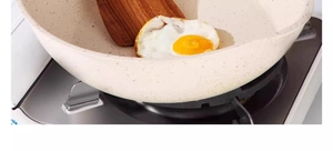 Close-up of a wooden spatula flipping a fried egg in a beige non-stick frying pan