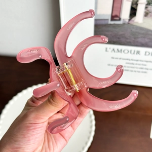 Pink 4mm thick octopus-shaped acetate hair claw clip held against a soft indoor background