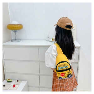 Detail view of a yellow school bus shaped kids chest bag worn in a cozy home setting
