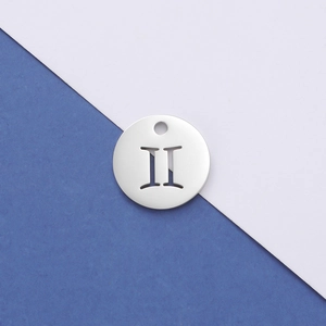Macro shot of silver Gemini zodiac pendant with hollow geometric cutout on two-tone paper