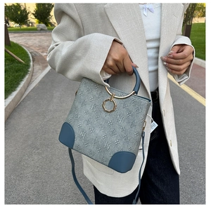 Detail of blue denim textured handbag with gold metal ring handle and monogram patterns