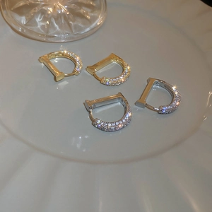 Gros plan de boucles d'oreilles en forme de D dorées et argentées avec zircons sur céramique