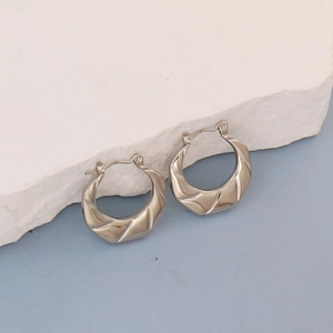 Detailed view of silver sculptural twisted hoop earrings resting on a white stone base