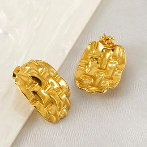 Polished gold geometric stud earrings with woven texture on a minimalist ceramic plate