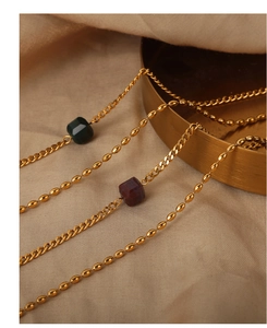 Macro detail of gold layering chain necklace with green and dark red square agate beads