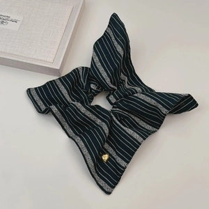 Détail d'un chouchou à rayures avec un pendentif cœur en métal et motifs géométriques