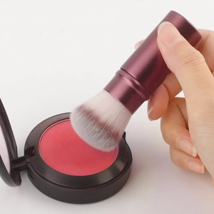Detail of burgundy retractable makeup brush applying red powder from a black compact