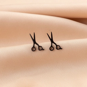 Detail shot of mini black scissor stud earrings on elegant champagne silk fabric