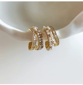 Detail of 14k gold plated C-shaped earrings with pearls and zircon in a luxury style