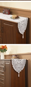 Detail view of white lace table runner featuring floral hollow patterns and tassel fringe