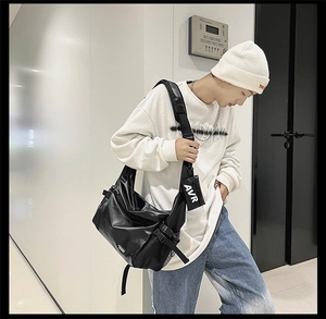 Detail of black crossbody bag with wide strap and AVR letter accessory on model
