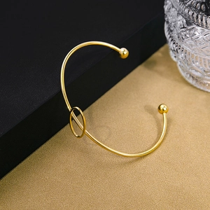 Detailed view of a gold-plated knot bangle on a black matte display box background