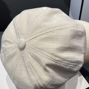 Macro detail of beige baker boy hat featuring textured jacquard fabric and top button
