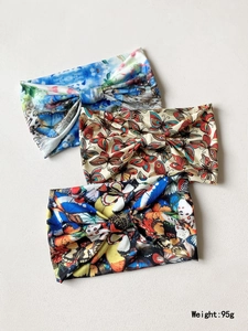 Three vibrant butterfly printed knotted headbands displayed on a textured neutral surface