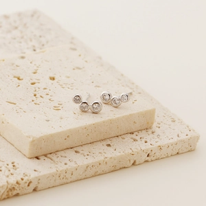 Close-up of S925 silver stud earrings with three bezel-set round diamonds on beige stones
