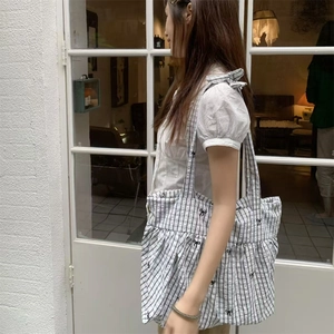 Detail of checkered tote bag featuring black bow patterns worn by model in street style