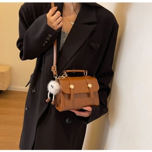 Brown leather envelope bag with plush charm on a model in a minimalist suit