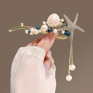 Détail de l'épingle à cheveux dorée avec étoile de mer en strass et pompons de perles