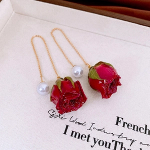 Detailed macro view of red rose bud earrings with dangling white pearl and gold chain