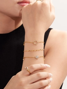 Nahaufnahme goldener Armbänder mit Kleeblatt-Anhänger und Zirkonia V-Ring