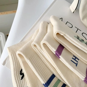 Détail de chaussettes en coton blanc avec rayures mauves et broderie de lettre HT