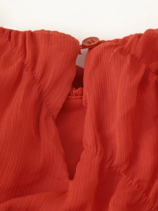 Close-up of red textured chiffon fabric featuring pleated details and a single button