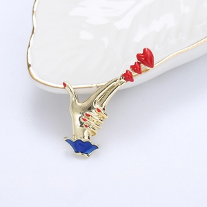 Detail shot of a golden hand brooch holding three red hearts on a white tray